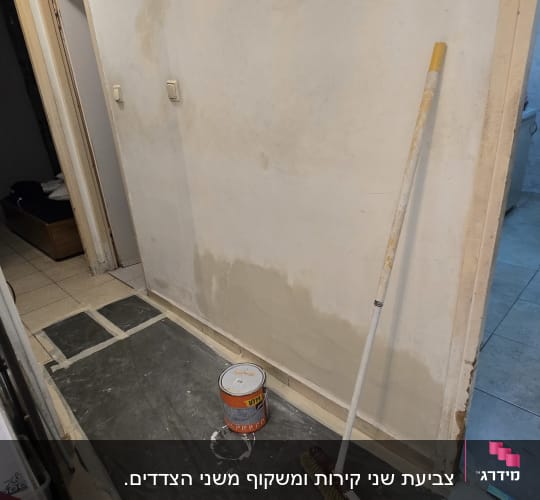 קיר צבוע חלקית עם מברשת ופח צבע על הרצפה